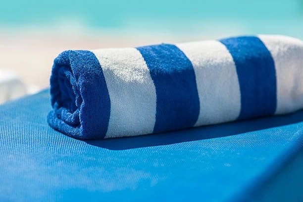 Rolled blue and white striped pool towel on a sun lounger with a blurred beach background